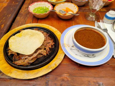 Birria adında lezzetli bir yemek, zengin bir çorba ve ahşap bir masada el yapımı tortilla ile servis edilir.