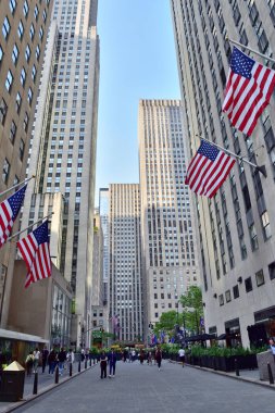 New York, ABD - 15 Mayıs 2023: Çok sayıda insanın yürüdüğü bir şehir caddesi. Cadde yüksek binalarla ve Amerikan bayraklı bayrak direğiyle dolu.