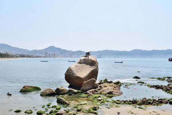 stock image Acapulco, Mexico - April 27 2024: A large rock sits on the beach next to the ocean. With a small statue called Narciso