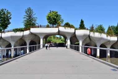 Yürüme yolu olan bir köprü ve suda kırmızı bir şamandıra. İnsanlar köprüde yürüyor.