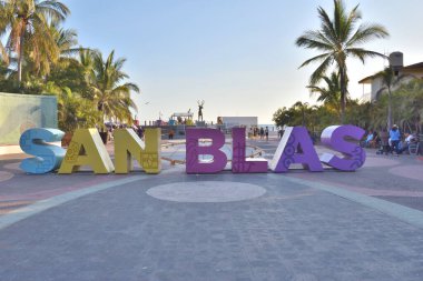 San Blas, Meksika - 25 Mayıs 2024 San Blas harflerinin renkli olduğu büyük bir tabela. Tabela, arka planda palmiye ağaçları ve plajı olan bir meydanda bulunuyor..