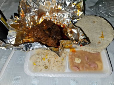 Michele adında bir tabak yemek. Tortilla ve fasulyenin üstünde taco var. Yemekler folyoyla kaplanmış.