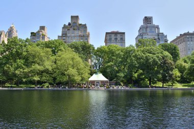 Ortasında yeşil çadır olan büyük bir su kütlesi. Su sakin ve gökyüzü berrak. Central Park New York