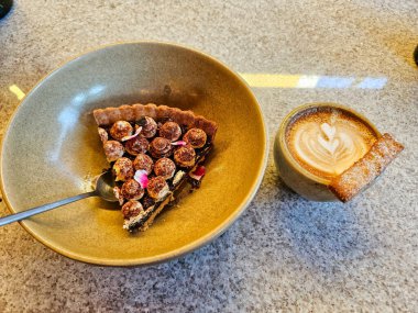 Tiramisu turtası sığ bir tabakta, bir restoranda cappuccino kahvenin yanında.