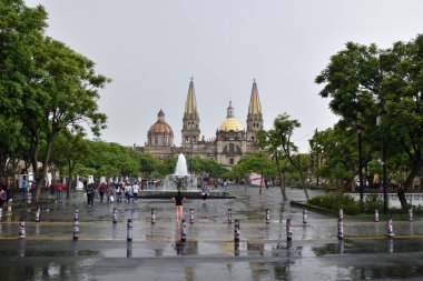 Guadalajara, Meksika 17 Ağustos 2024: Meksika 'nın Guadalajara şehrinin tarihi merkezinde, ikonik katedralin ve ağaçlarla çevrili merkezi bir çeşmenin yer aldığı yağmurlu bir gün
