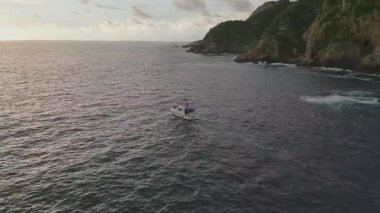 Acapulco kayalıklarının yakınındaki sularda uçan bir teknenin güzel bir gün batımında insansız hava aracı tarafından yakalanması.