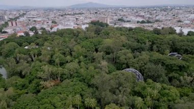 Guadalajara 'daki Agua Azul Parkı üzerinde geriye doğru uçan bir insansız hava aracı videosu yemyeşil ve kentsel manzarasını gözler önüne seriyor.
