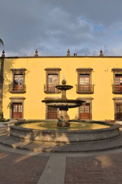 Zapopan, Meksika - 8 Haziran 2024: Zapopan, Meksika 'da sömürge tarzı sarı binalı halka açık bir meydanda klasik bir taş çeşmesi