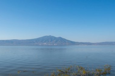Chapala Gölü 'nün sakin suları ve Jalisco Ajijic' ten görünen dağlık manzarası berrak gökyüzü altında.