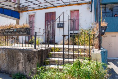 Metal parmaklıkları, tahta kapıları ve güçlü güneş ışığı altında kentsel bir çevrede kurumuş bitkileri olan terk edilmiş eski bir ev.