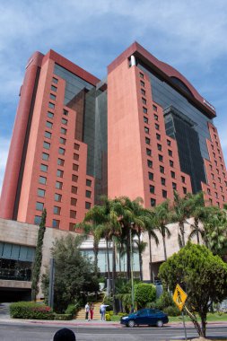 Guadalajara, Meksika - 4 Mayıs 2025: Guadalajara 'da palmiye ağaçları ve mavi gökyüzü olan çağdaş kırmızı otel kulesi