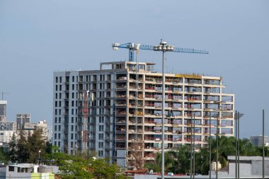 Zapopan, Meksika - 5 Haziran 2025: Şehir yapıları tarafından çevrelenmiş, inşaat halindeki yüksek katlı beton bina ve kentsel alandaki kule vinci