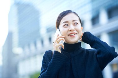 Asyalı kadın dışarıda akıllı telefondan konuşuyor.