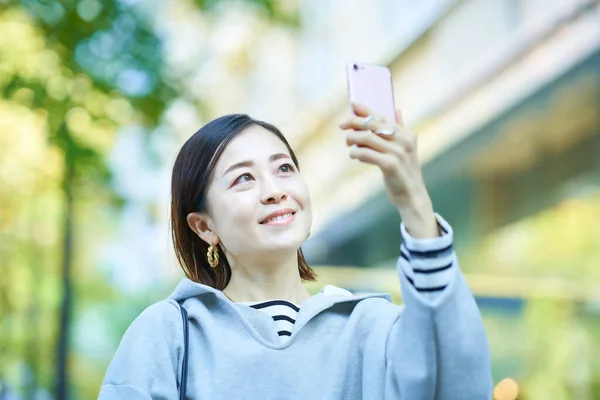Młoda Kobieta Trzyma Smartfona Zewnątrz — Zdjęcie stockowe
