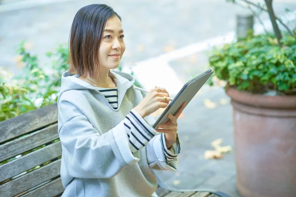身穿休闲装的亚洲妇女操作平板电脑 — 图库照片