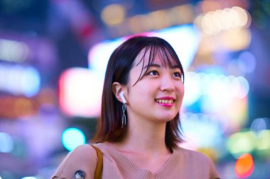 Asyalı genç bir kadın gece şehir merkezinde duruyor.