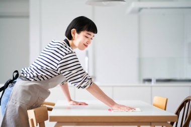 Genç bir kadın yemek masasını siliyor.