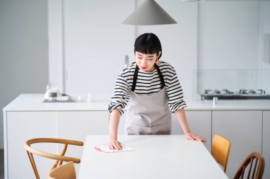 Genç bir kadın yemek masasını siliyor.