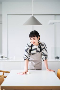 Genç bir kadın yemek masasını siliyor.