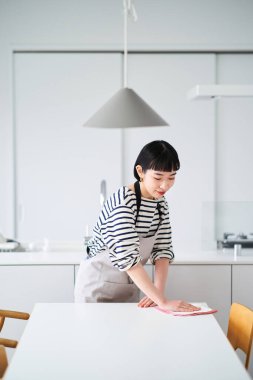 Genç bir kadın yemek masasını siliyor.