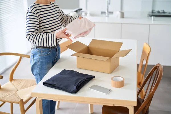 Young woman packing clothes into cardboard in the room