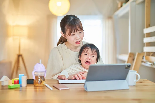 A woman who operates a tablet PC and a crying infant at home