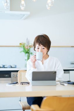 Odanın mutfağında internetten iletişim kuran bir kadın.