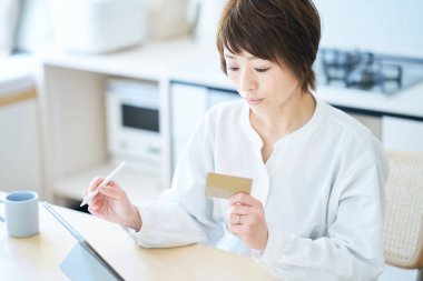 Odada elinde bir kart tutan ve tablet bilgisayar kullanan bir kadın.