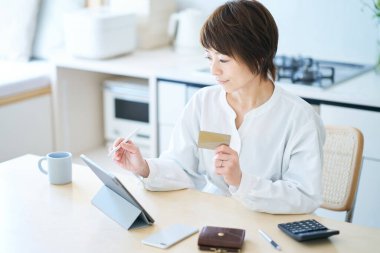 Odada elinde bir kart tutan ve tablet bilgisayar kullanan bir kadın.