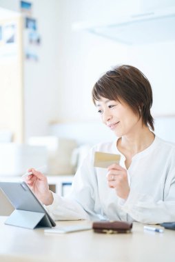 Odada elinde bir kart tutan ve tablet bilgisayar kullanan bir kadın.