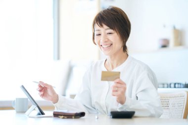 Odada elinde bir kart tutan ve tablet bilgisayar kullanan bir kadın.