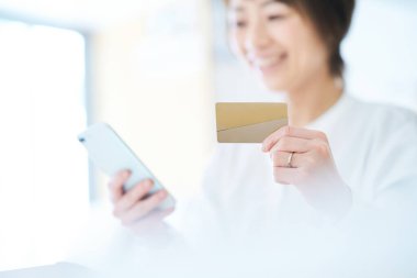 Elinde kart tutan ve odada akıllı telefon kullanan bir kadın.