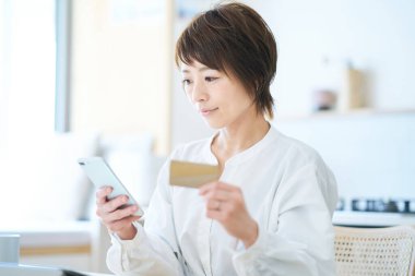 Elinde kart tutan ve odada akıllı telefon kullanan bir kadın.