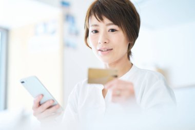 Elinde kart tutan ve odada akıllı telefon kullanan bir kadın.