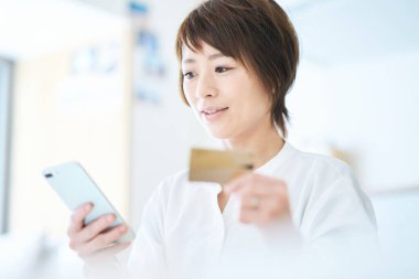 Elinde kart tutan ve odada akıllı telefon kullanan bir kadın.