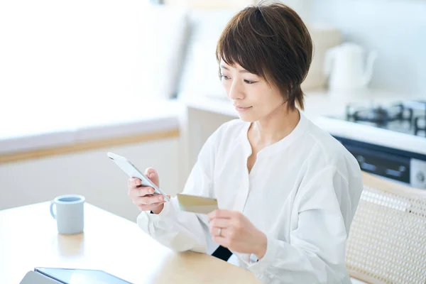 A woman holding a card and operating a smartphone in the room