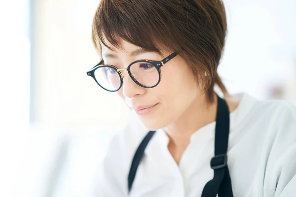 A woman in an apron wearing glasses in the room