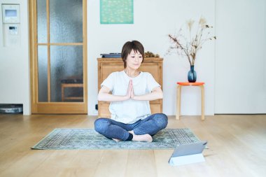 Tablet bilgisayar ekranına bakarken odada gerinen bir kadın.