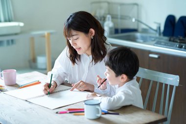 Anne ve çocuk odada kalem ve defterle ders çalışıyor.