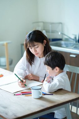 Anne ve çocuk odada kalem ve defterle ders çalışıyor.