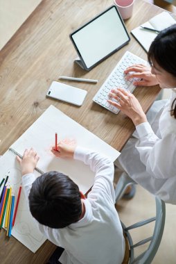 Odasında çalışan bir anne ve çizim yapan bir çocuk.