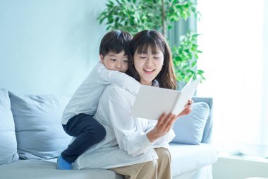 Anne ve çocuk kanepede oturup resim kitabı okuyorlar.