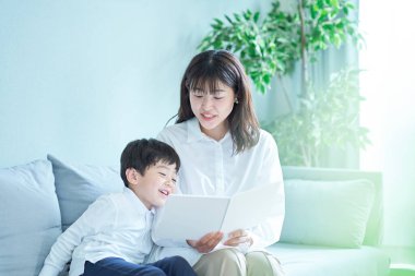 Anne ve çocuk kanepede oturup resim kitabı okuyorlar.