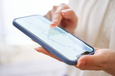 Bir kadın odasındaki akıllı telefonuyla döviz çizelgesini kontrol ediyor.
