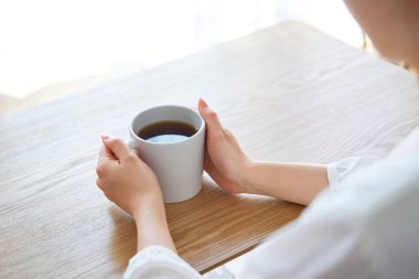 Bir kadının eli fincanı tutuyor ve odada düşünüyor.