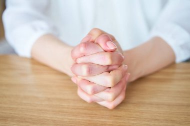 Ellerini odada kavuşturup düşünen bir kadının elleri.