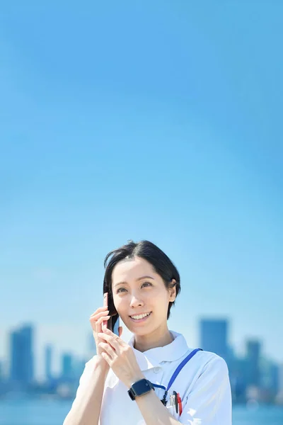 Beyaz Önlüklü Bir Kadın Dışarıda Akıllı Telefon Tutuyor — Stok fotoğraf