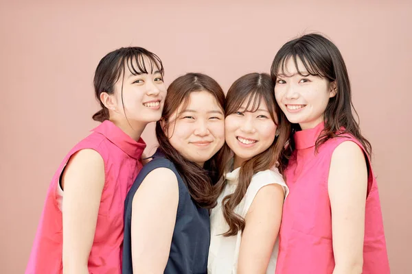 A group of four young women standing in front of a color background