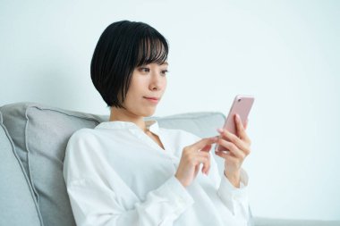 Kanepede oturan ve odada akıllı telefon kullanan bir kadın.