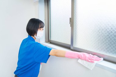 İş kıyafetleri ve maskeli bir kadın odayı temizliyor.